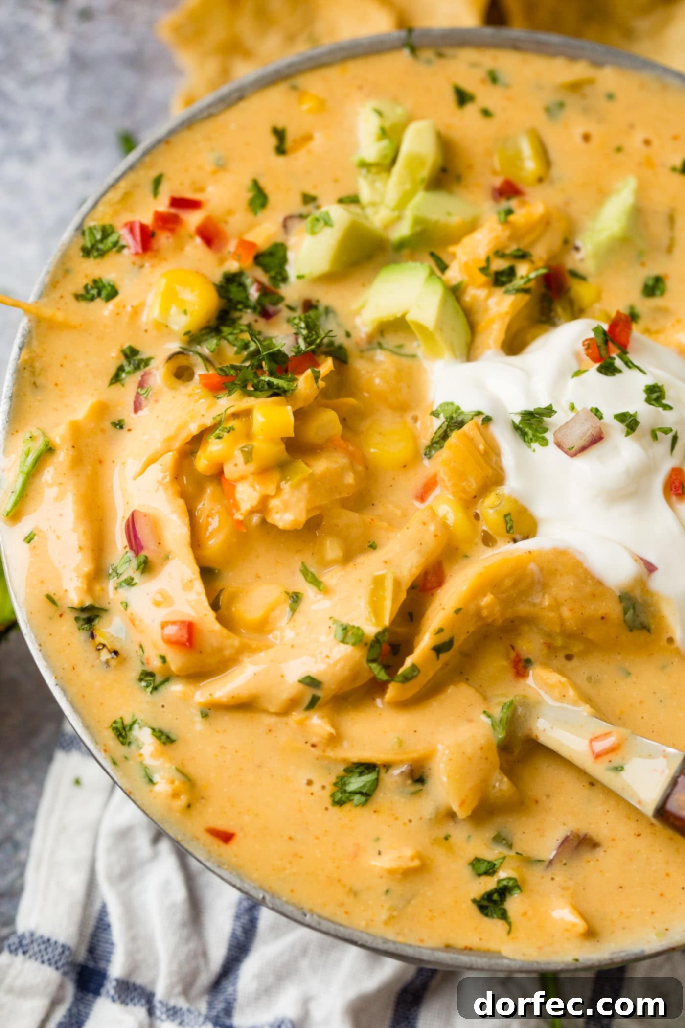 A vibrant bowl of cheesy southwest chicken soup, garnished generously with fresh sour cream and slices of ripe avocado.