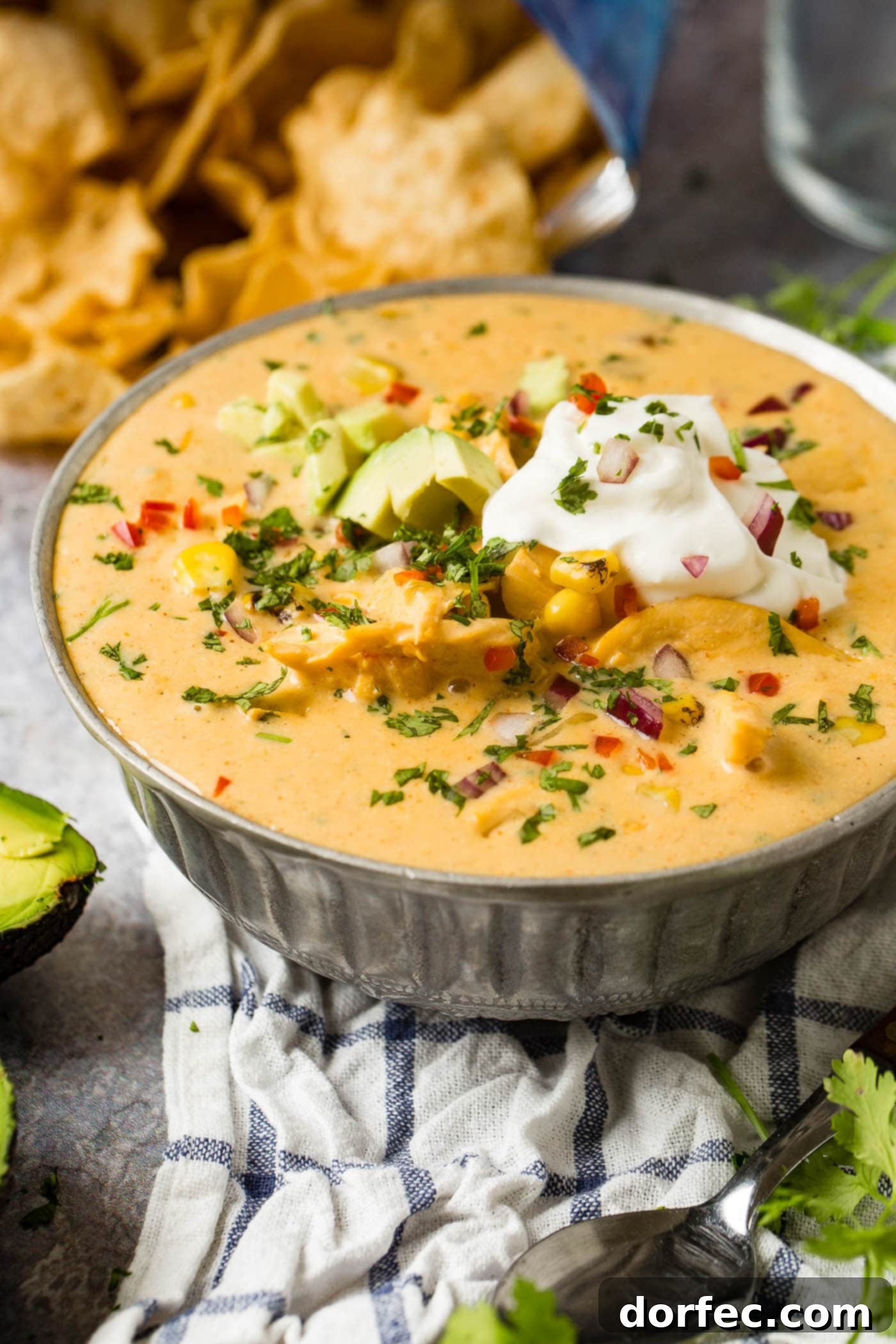 A close-up shot of a steaming bowl of cheesy chicken tortilla soup, adorned with a swirl of sour cream and fresh avocado slices, ready to be enjoyed.