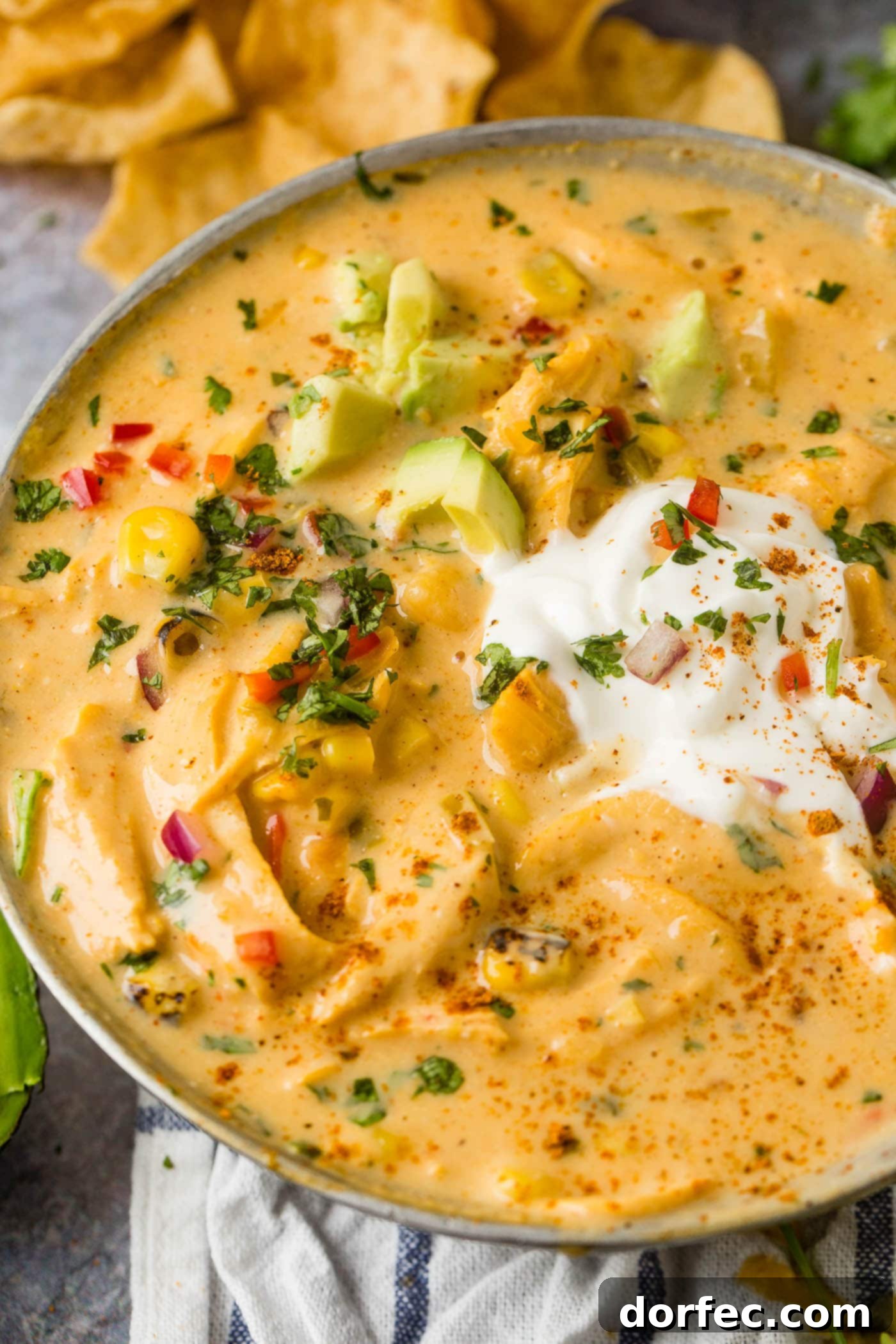 A beautifully presented bowl of cheesy chicken tortilla soup, topped with fresh sour cream and sliced avocados, highlighting its inviting and rich texture.