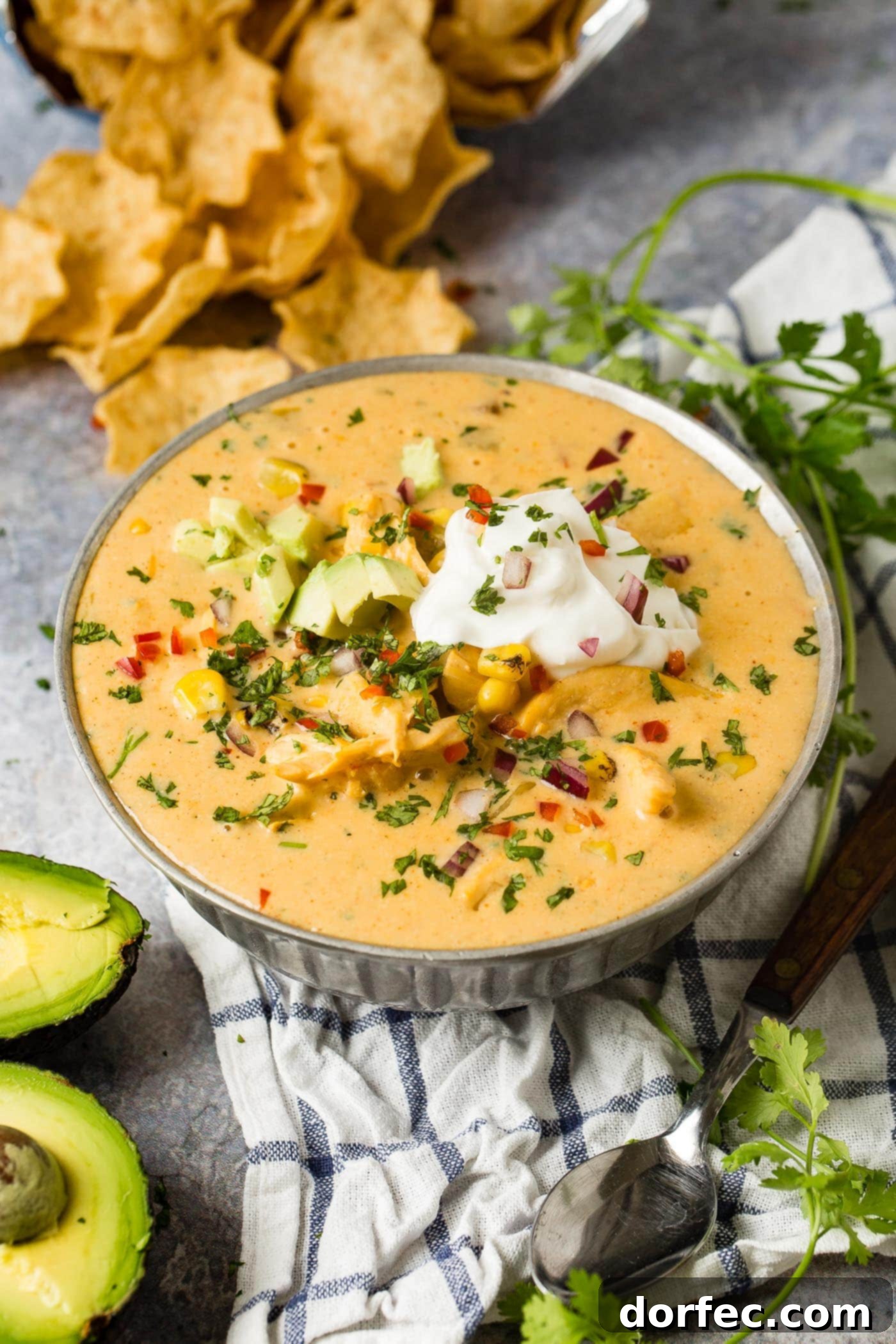 An enticing bowl of cheesy chicken tortilla soup, beautifully presented with a dollop of sour cream and fresh avocado, showcasing its rich and comforting appeal.