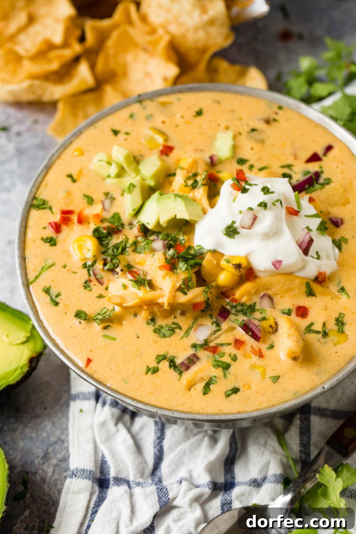 A inviting bowl of cheesy southwest chicken soup, beautifully garnished with fresh sour cream and ripe avocado slices, ready to be enjoyed.