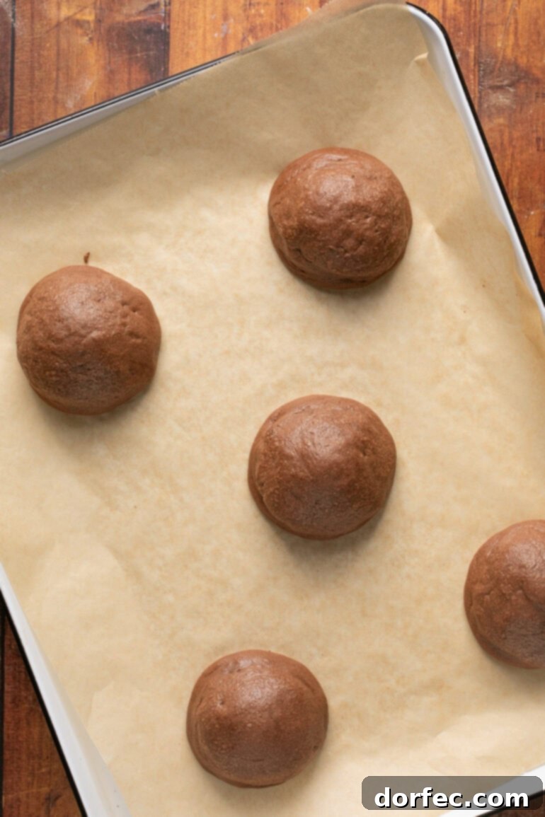 A close-up shot of a single, large marshmallow being placed carefully on top of a partially baked chocolate cookie on a parchment-lined baking sheet, preparing it for the final bake.