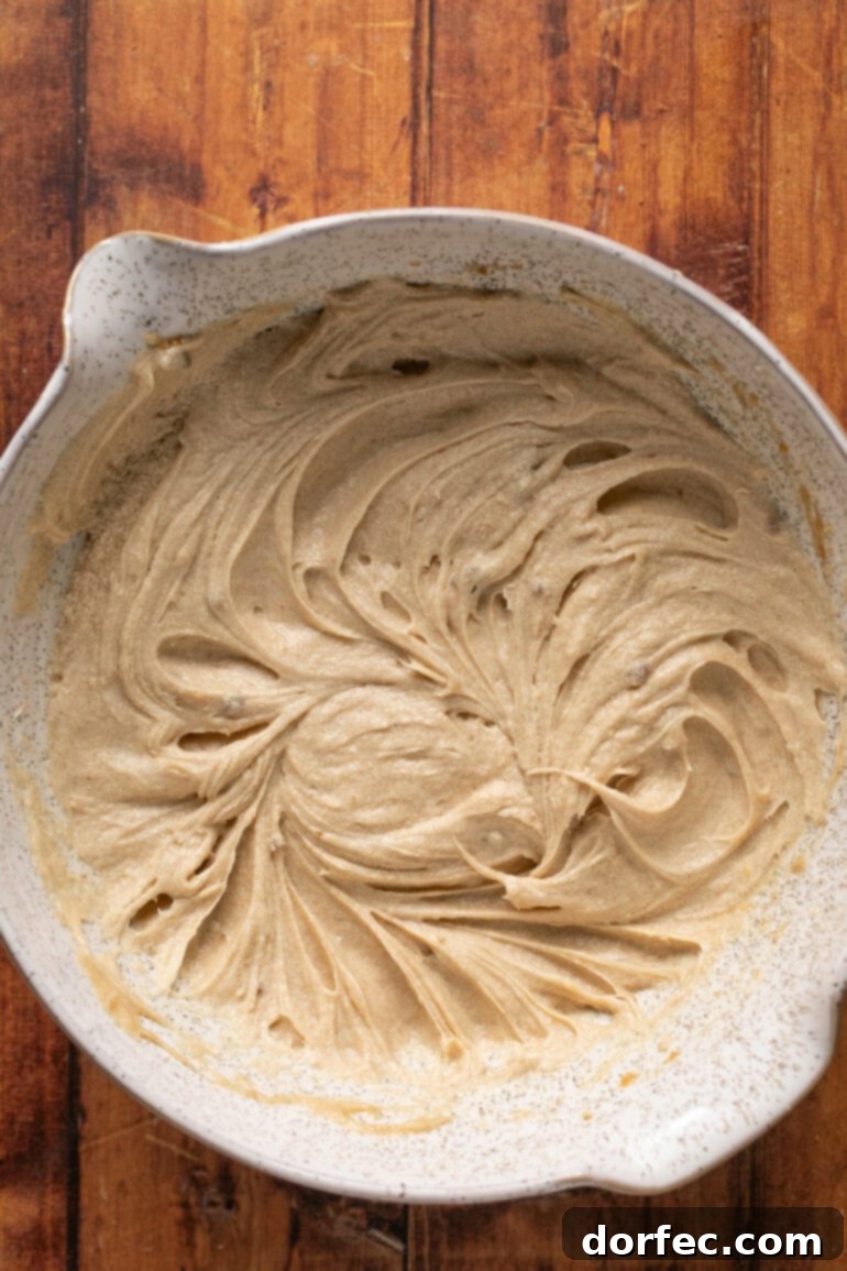 A clear photo showing large eggs being added to the creamed butter and sugar mixture, ready for whisking to incorporate them smoothly into the cookie dough.