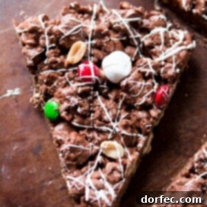 Close-up of a festive M&M Chocolate Pizza slice, featuring colorful candies, peanut butter chips, and fluffy marshmallows.