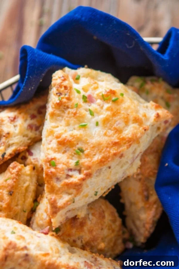 A golden-brown savory ham and cheese scone, perfectly flaky, resting on a stack of other scones.
