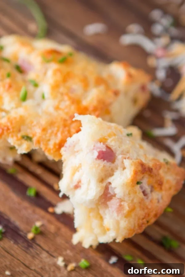 A close-up of a tender, flaky ham and cheese scone on a wooden cutting board, revealing its soft interior and savory fillings.