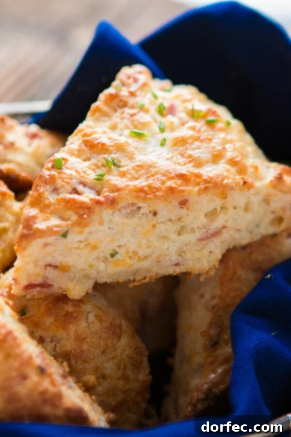 A delicious close-up of a golden, fluffy ham and cheese scone, topped with melted butter and fresh chives, showcasing generous chunks of ham and cheese within.