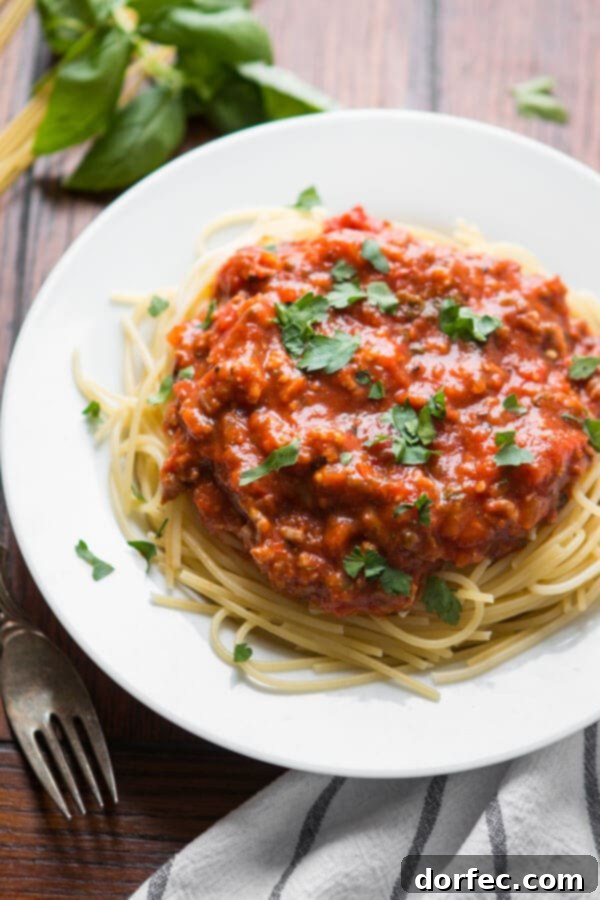 spaghetti topped with homemade pasta sauce sprinkled with chopped parsley on a white plate