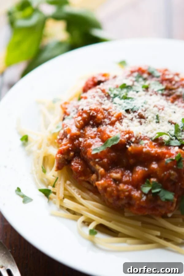best homemade spaghetti sauce atop pasta on white plate topped with grated parmesan and chopped parsley