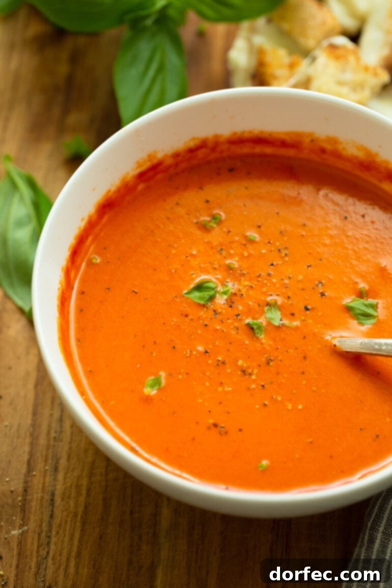 Roasted Tomato Basil Soup with Grilled Cheese Bites 5 A heartwarming close-up of a bowl of homemade tomato basil soup, showcasing its vibrant orange-red hue and generously topped with fresh minced basil and cracked black pepper, ready for a cozy fall day.