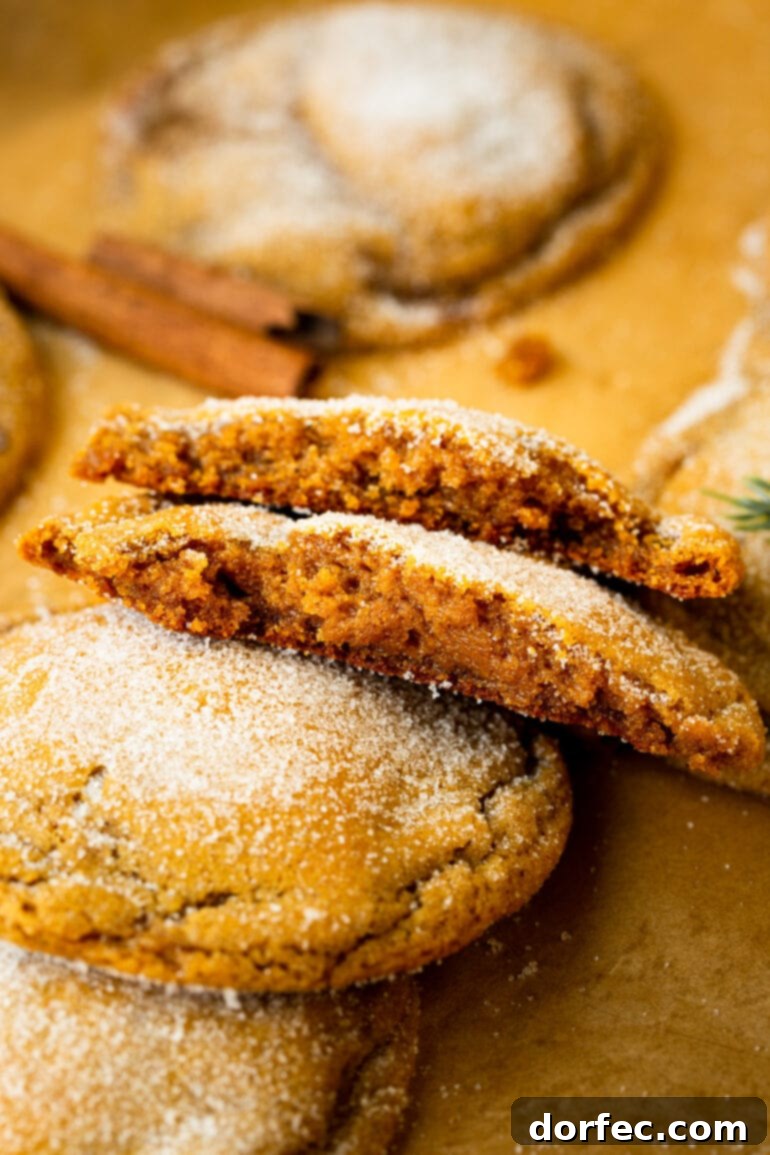 A photograph of a stack of freshly baked, chewy molasses cookies, with two broken in half to reveal their soft, moist centers.