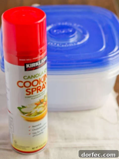 A Tupperware container being sprayed with nonstick cooking spray before food storage, illustrating how to prevent future stains from tomato-based sauces.