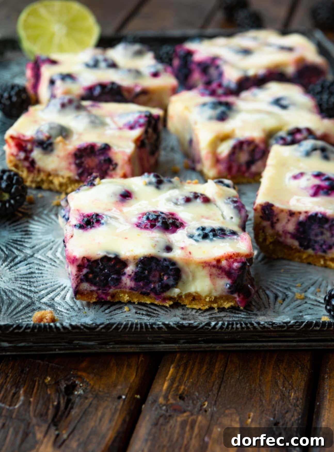 Effortless Blackberry Lime Bars 3 A serving tray displaying several perfectly sliced blackberry lime bars, each showcasing its golden graham cracker crust, creamy lime filling, and juicy purple blackberries.