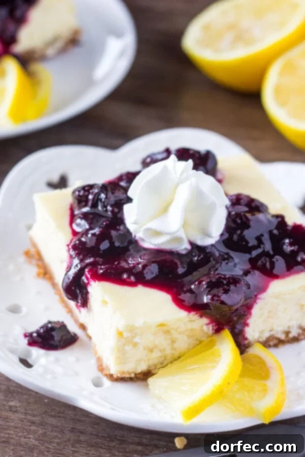Delicious Lemon Blueberry Cheesecake Squares Rich lemon blueberry cheesecake squares on a serving plate, topped with fresh blueberry sauce