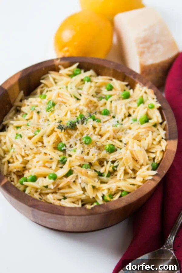 A small wooden bowl featuring homemade quick and easy lemon orzo pasta with parmesan and peas, artfully arranged next to fresh lemons and wedges of Parmesan cheese on a rustic surface.