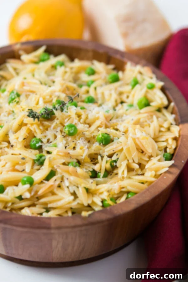 A rustic wooden bowl of simple lemon orzo pasta with parmesan and peas, perfectly plated alongside a vibrant red cloth napkin, ready to be served.