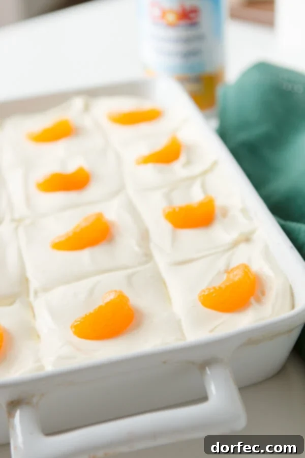 Homemade Orange Jello Fruit Salad with Lemon Topping A large white baking dish filled with vibrant orange jello fruit salad, topped with a creamy lemon layer and garnished with mandarin oranges.