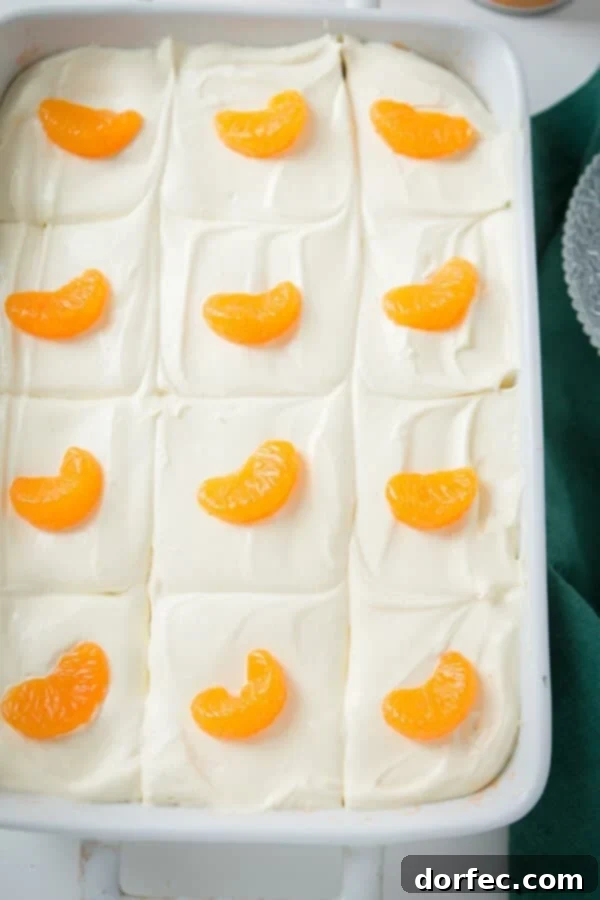 Delicious Mandarin Orange Jello Salad with Lemon Cream A close-up of the bright orange jello salad in a white baking dish, showing the creamy lemon topping and glistening mandarin orange segments.