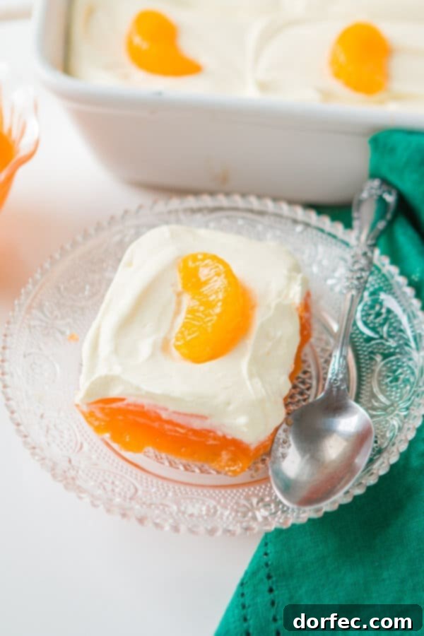 Ready-to-Serve Lemon Mandarin Orange Jello Salad A delicious slice of lemon mandarin orange jello salad on a clear glass plate, accompanied by a spoon, ready to be enjoyed.