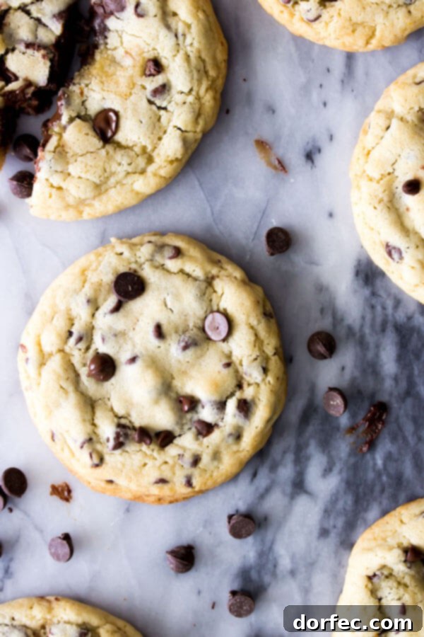 An overhead shot of several golden-baked chocolate chip cookies, one of which is broken open to reveal the rich, melty fudge filling oozing out