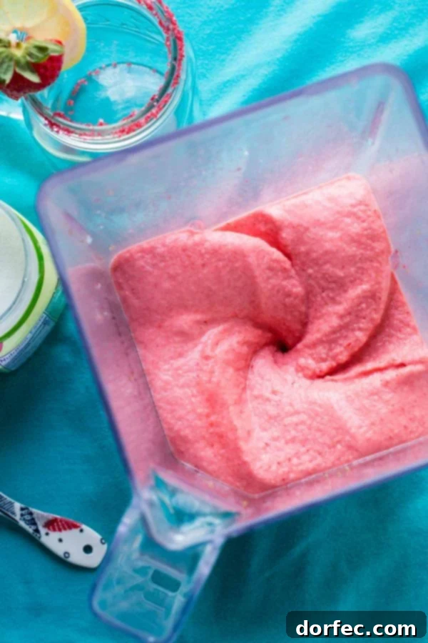 Quick and Easy Frozen Strawberry Lemonade Recipe A close-up of the frozen strawberry lemonade's smooth, icy consistency, showing flecks of real strawberry in a clear glass with a cheerful straw.