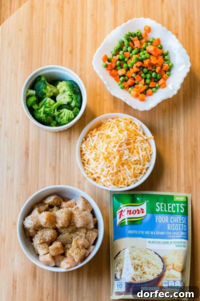 Overhead view of six simple ingredients laid out for Cheesy Chicken and Rice Casserole: Knorr Selects Four Cheese Risotto, chicken breasts, poultry seasoning, broccoli, peas and carrots, and Colby Jack cheese.