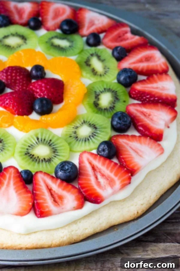 Colorful sugar cookie fruit pizza topped with a vibrant array of fresh strawberries, blueberries, kiwi, and mandarin oranges, making it a perfect spring or summer dessert