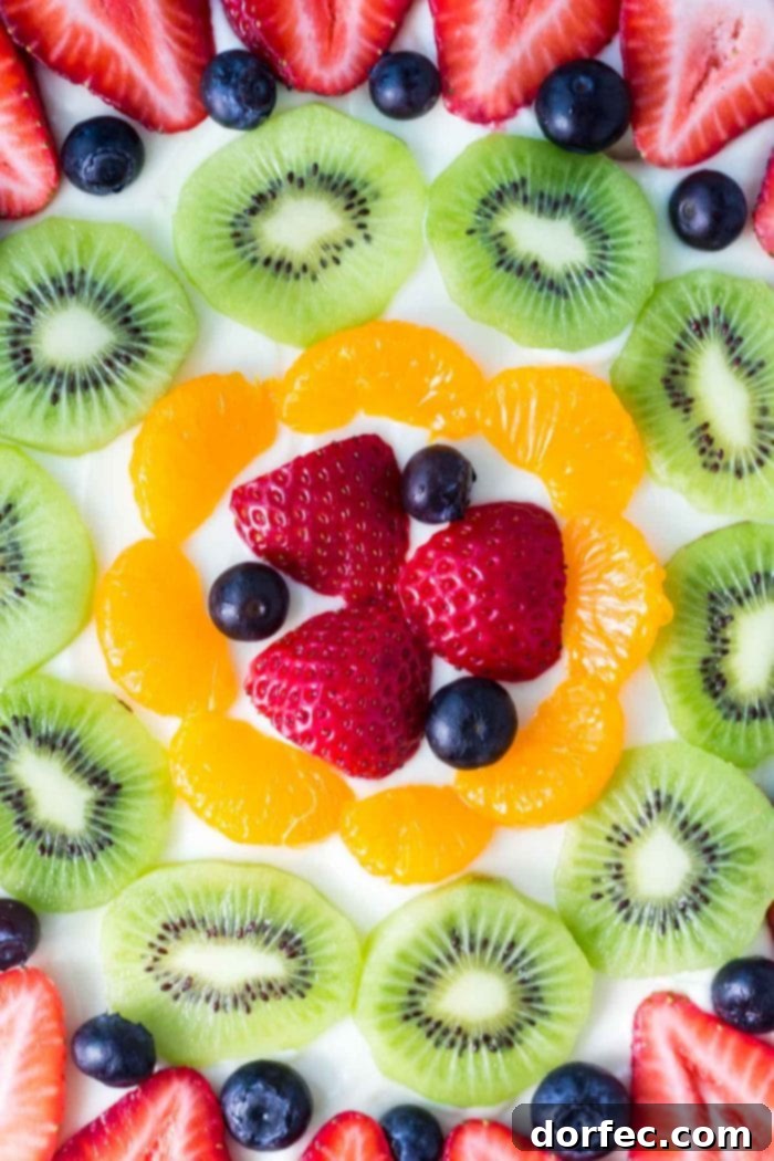 Overhead shot of a full sugar cookie fruit pizza adorned with a beautiful pattern of fresh fruit including strawberries, kiwi, blueberries, and mandarin oranges.