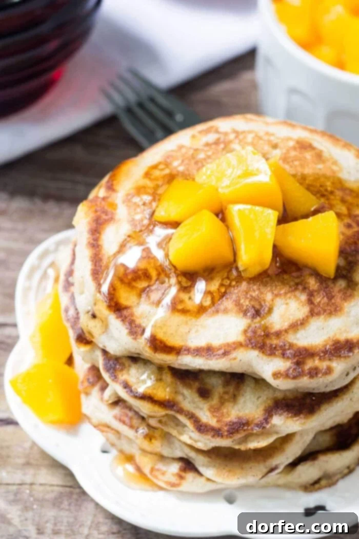 Freshly Stacked Peach Pancakes with Diced Peaches on Top Close-up of a stack of golden peach pancakes on a white plate, topped with a generous amount of fresh, diced peaches. The light, airy texture of the pancakes is visible, inviting a spoonful of sweet summer flavor.