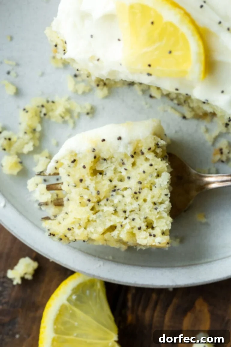 Zesty Lemon Poppy Seed Cake with Velvety Cream Cheese Frosting 3 a photo of a bite of lemon poppy seed cake sitting on a fork laying on a plate next to a slice of the cake