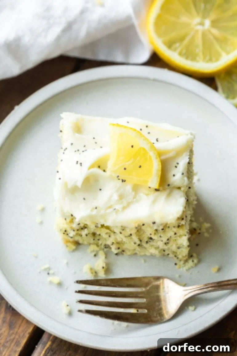 Zesty Lemon Poppy Seed Cake with Velvety Cream Cheese Frosting 4 a photo of a slice of lemon poppy seed cake sitting on small white dessert plate topped with a smooth cream cheese frosting and a thin slice of lemon