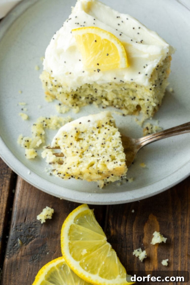 Zesty Lemon Poppy Seed Cake with Velvety Cream Cheese Frosting 6 a photo of a bite of lemon poppy seed cake on a fork and sitting next to a slice of cake