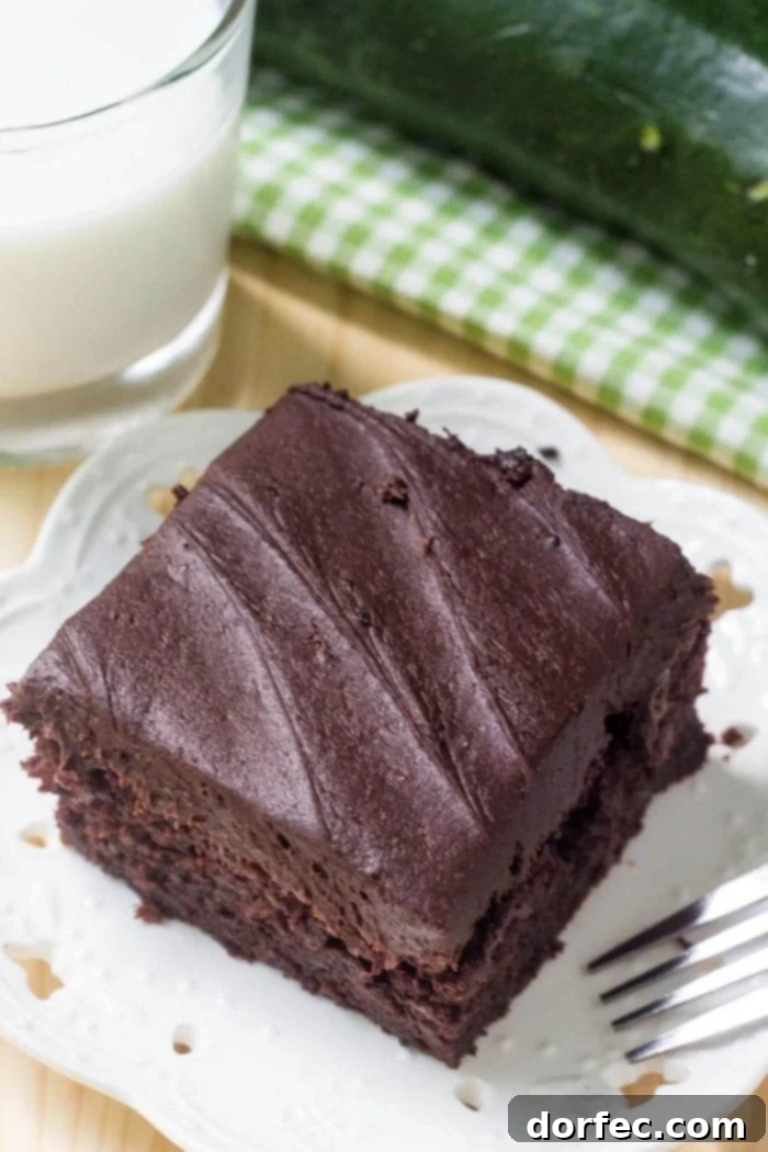An overhead view of a delicious slice of double chocolate zucchini cake on a white plate, paired with a glass of milk, showcasing its inviting texture.