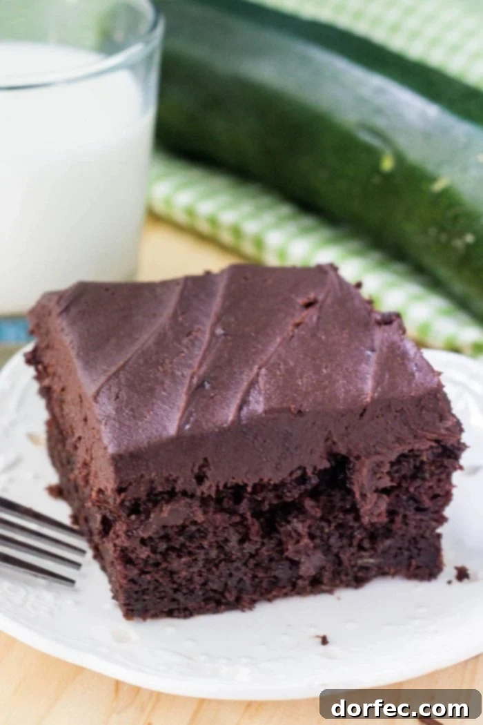 A beautifully sliced double chocolate zucchini cake on a white plate, artfully placed beside a glass of milk, beckoning for a taste.