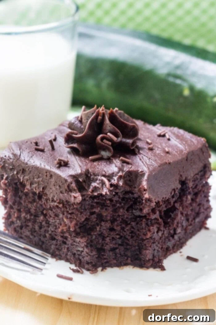 A tempting slice of frosted double chocolate zucchini cake on a white plate, presented alongside a glass of milk.
