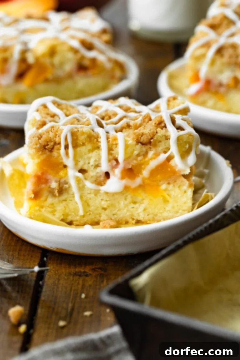 A slice of golden peach coffee cake, generously topped with a crumbly streusel and a luscious white vanilla drizzle, presented on a small dessert plate.