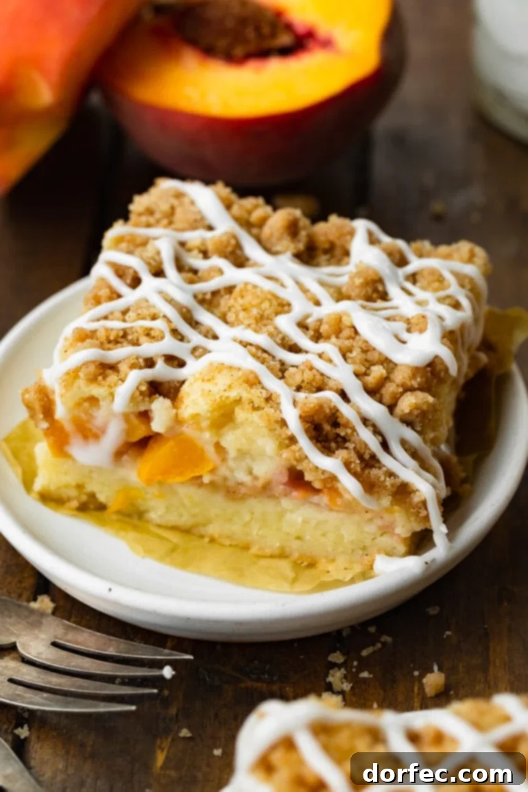 A large, inviting slice of peach coffee cake sits on a small dessert plate, showcasing its golden crumb, generous streusel topping, and glistening vanilla glaze drizzle.
