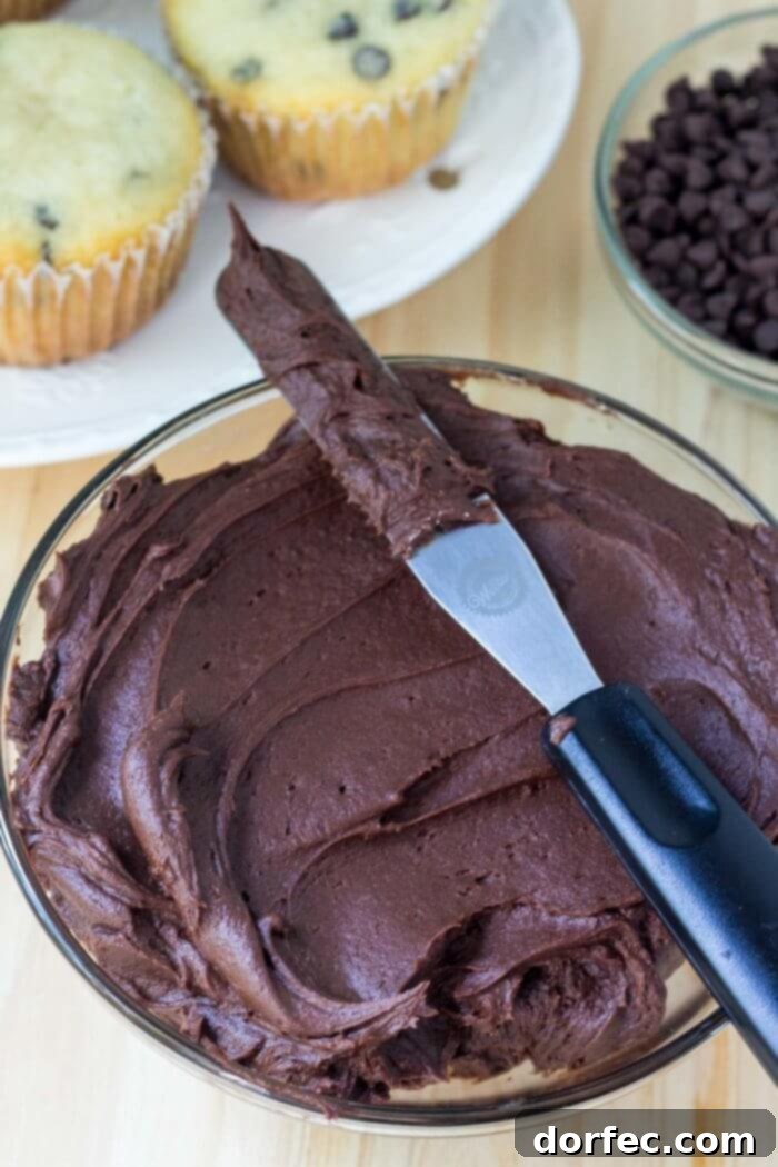 Rich, creamy chocolate frosting being swirled onto a vanilla cupcake.