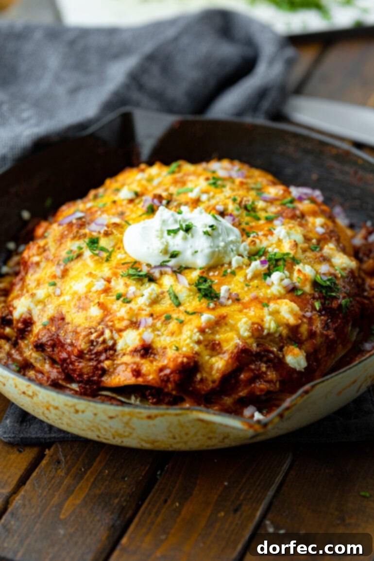 Quick One Skillet Ground Beef Enchilada Dinner 9 A large cast iron skillet filled with layers of ground beef enchilada casserole, generously topped with melted cheese and a dollop of sour cream, ready to serve a crowd.