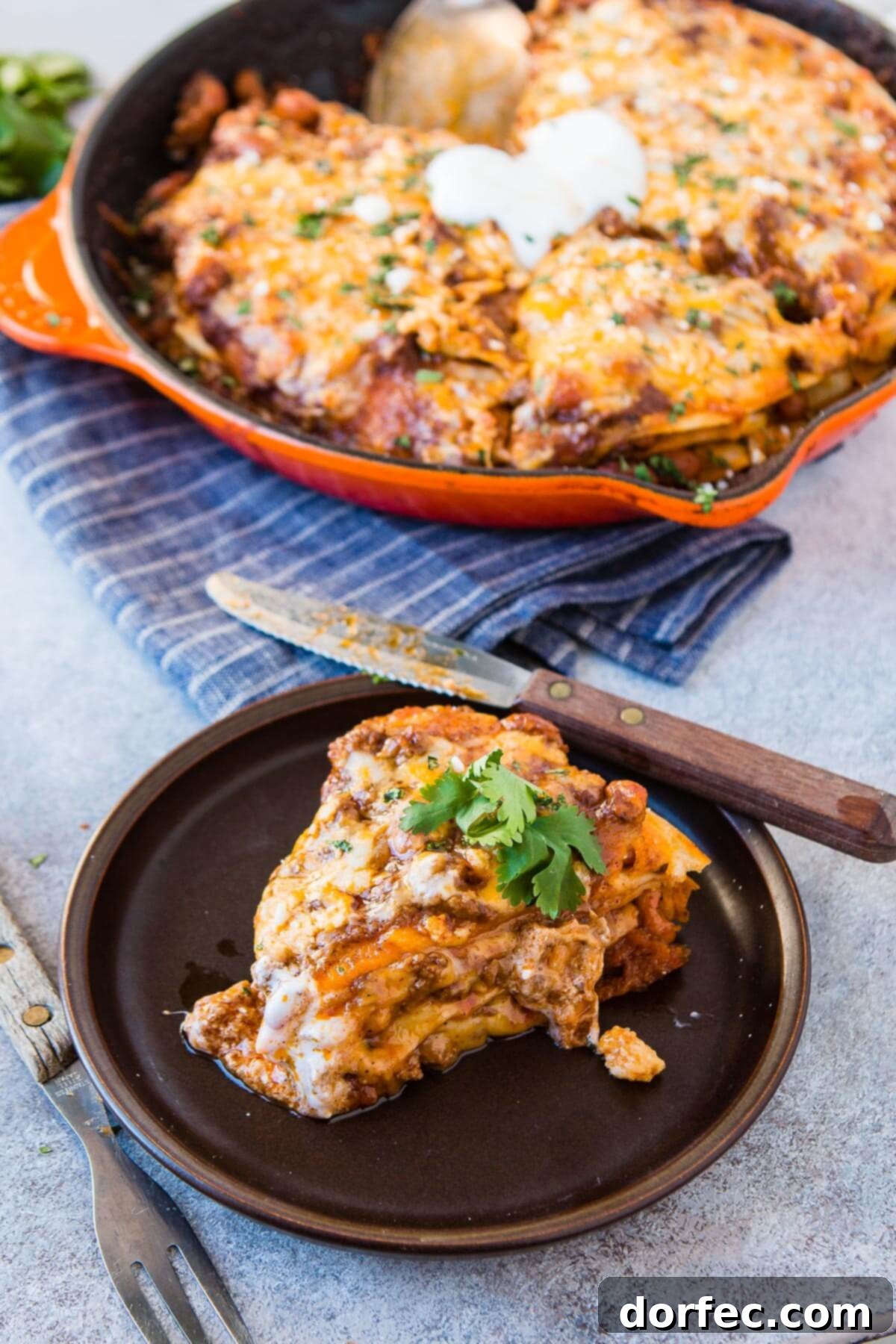 Quick One Skillet Ground Beef Enchilada Dinner 10 A delicious slice of ground beef enchilada casserole on a dinner plate, with the full skillet of casserole blurred in the background, inviting you to dig in.