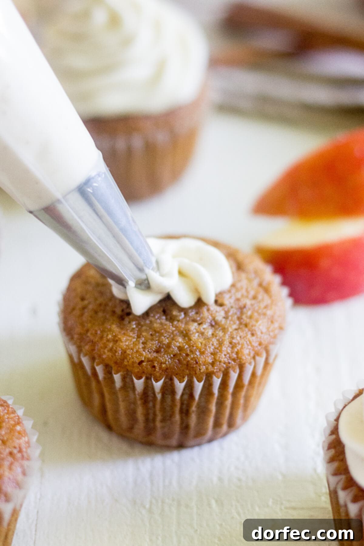 piping creamy cinnamon cream cheese frosting onto a freshly baked apple cupcake, ready for autumn enjoyment