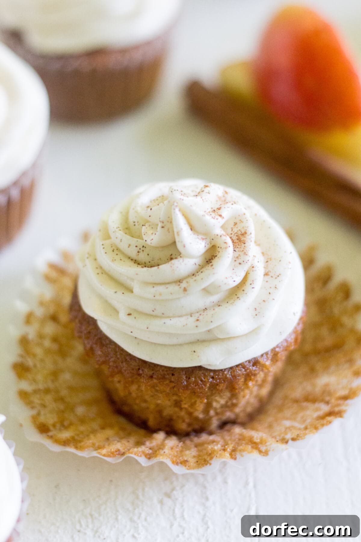 a single apple cider cupcake generously frosted with a swirl of cinnamon cream cheese, its liner peeled back invitingly