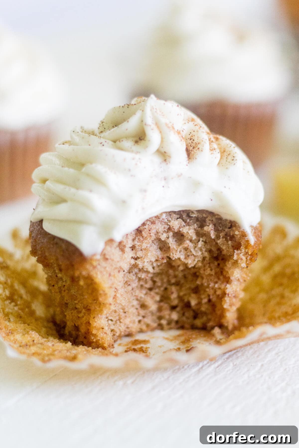 an apple cinnamon cupcake with a bite taken out, revealing the soft interior and creamy frosting