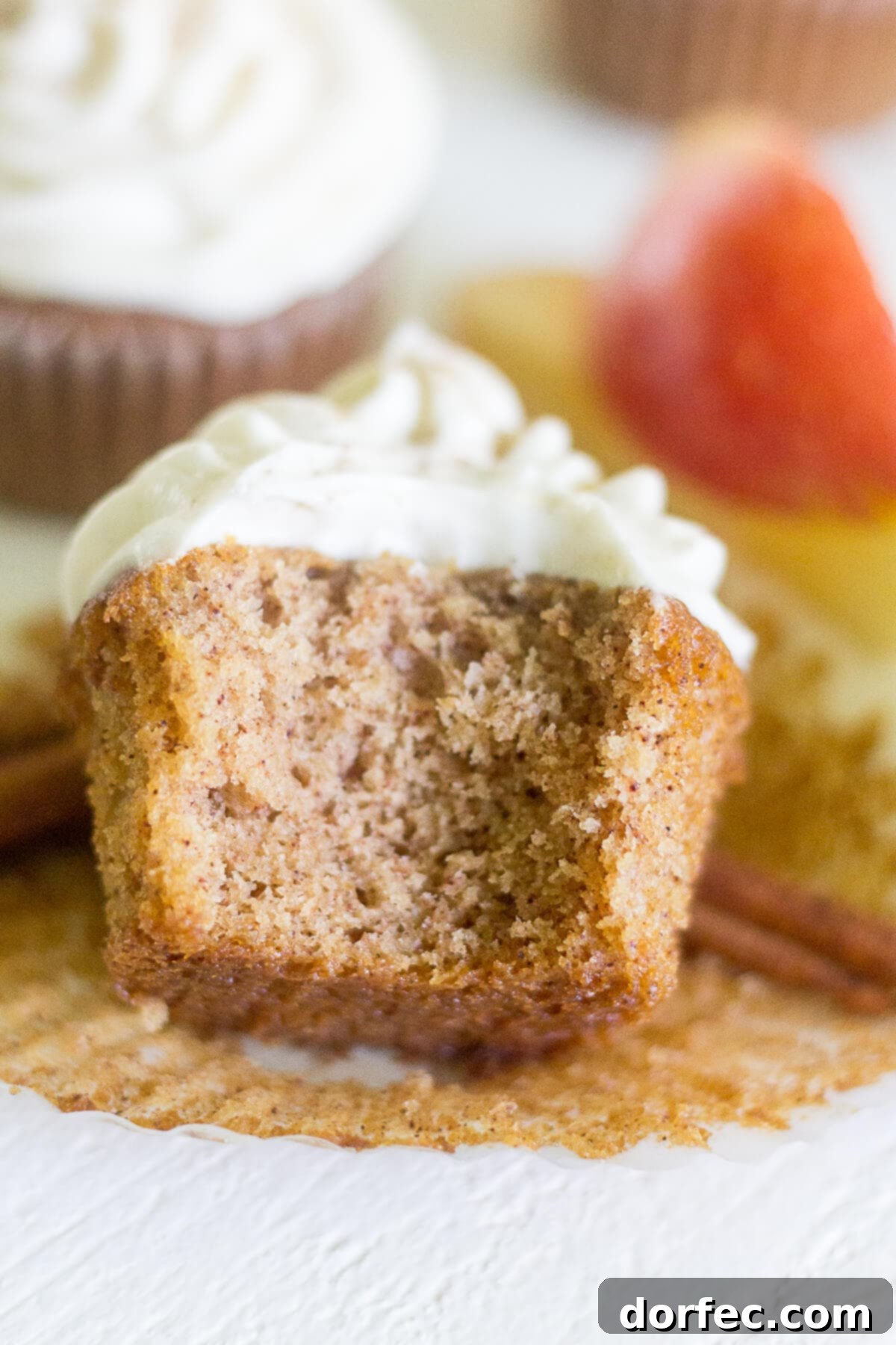 an apple cinnamon cupcake resting on its side with a bite taken, showcasing its moist texture and rich frosting