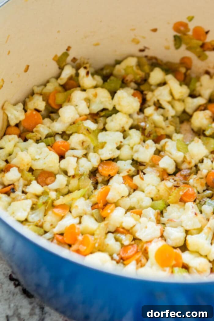 Sautéing diced carrots, onion, celery, and cauliflower in a Dutch oven until tender, preparing them for a creamy and delicious chowder.