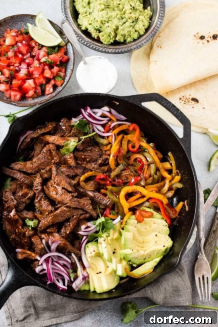 The Ultimate Steak Fajita Marinade 5 Overhead view of steak fajitas with peppers and onions, tortillas, salsa, and guacamole on the side, creating a vibrant spread.
