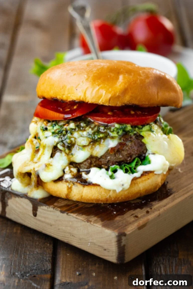 a photo of a garlic pesto burger topped with melted havarti cheese, pesto, bright red tomatoes all on a brioche bun.