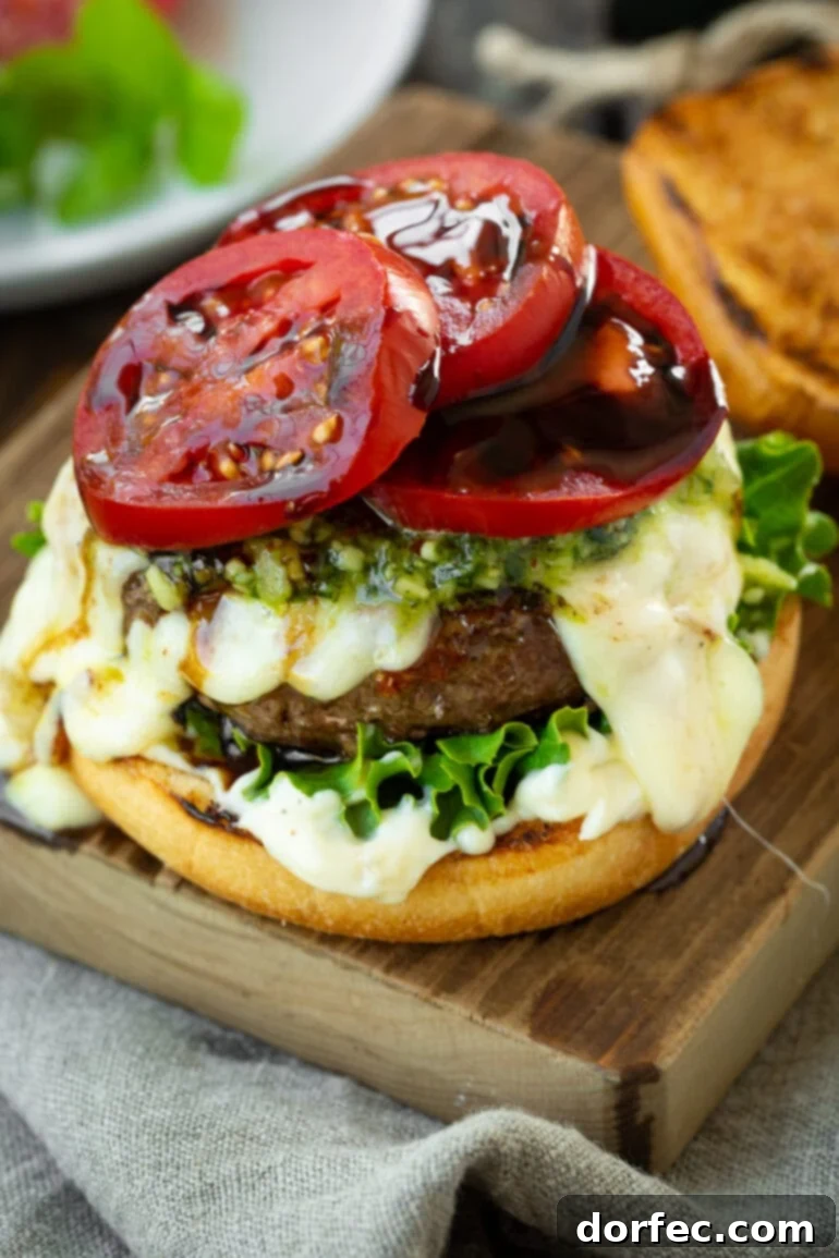 a photo of a garlic pesto burger with the top bun missing so you can see the tomato slices dripping with balsamic glaze