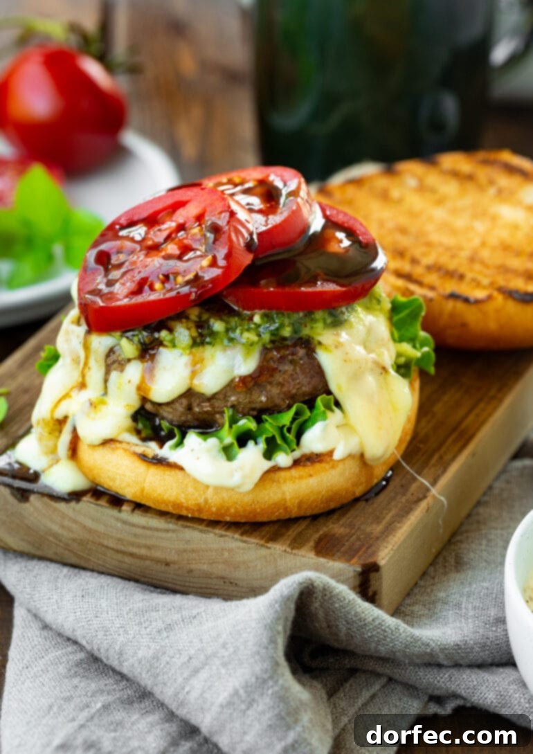 a photo of a garlic pesto caprese burger with the top bun off so you can see the bright red tomato slices drizzled with balsamic glaze.