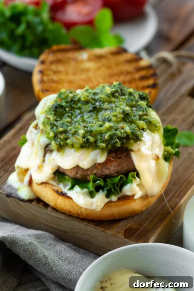 a photo of a burger with the top bun removed with a garlic aioli, green leave lettuce, melted havarti cheese and bright green pesto on top. 
